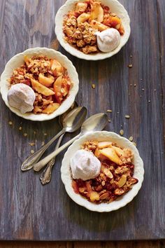 three bowls filled with food sitting on top of a wooden table next to spoons