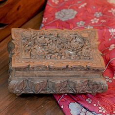 an old wooden box sitting on top of a red and pink cloth covered tablecloth