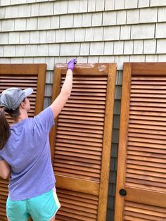 a woman painting wooden shutters on the side of a house