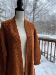 an orange cardigan sweater on a mannequin in front of snow covered trees