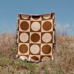 a brown and white blanket sitting on top of a grass covered field next to tall dry grass