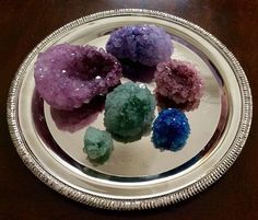 four different colored rocks in a silver plate on a wooden table with beaded edge