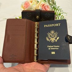 a person holding an open passport in front of a flower vase with flowers behind it