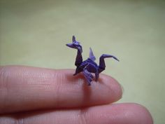 a tiny purple origami dragon sitting on someone's finger