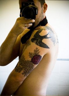 a man with tattoos taking a selfie in front of a mirror while holding a camera