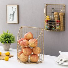 some apples are in a wire basket on the counter next to plates and utensils