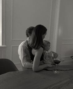 two women sitting at a table with wine glasses in front of them, one holding the other