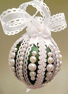 an ornament hanging from the ceiling with white ribbon and pearls on it's side