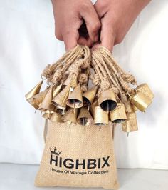 a bag filled with lots of gold bells on top of a white table next to a person's hand