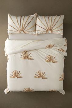 an image of a bed with white sheets and gold embroidered sunbursts on it