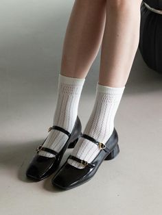 a woman in black shoes and white socks with her legs crossed, sitting on a suitcase