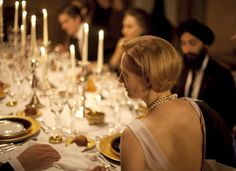 a man and woman sitting at a dinner table with candles on the tables behind them