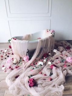 a bathtub with flowers on the floor and petals all over it, in front of a white wall