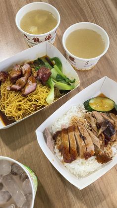 two takeout boxes filled with food on top of a wooden table next to bowls of soup