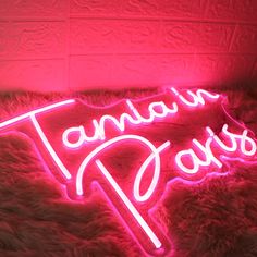 a pink neon sign that says taman in paris on top of a furry surface