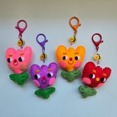 four different colored stuffed animals hanging from keychains on a white surface with clippings in the shape of hearts