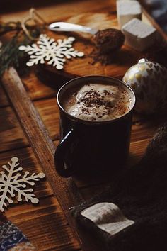 a cup of hot chocolate sitting on top of a wooden table covered in snowflakes