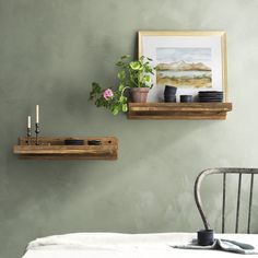 two wooden shelves on the wall above a bed with a plant and candle holder next to it