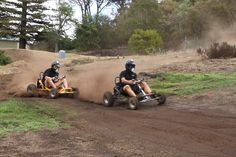 two people riding on four wheelers in the dirt