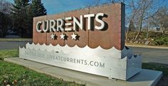 a sign that is in front of some grass and trees with the words currents written on it