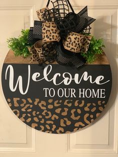 a welcome to our home sign hanging on a door with leopard print and black bow