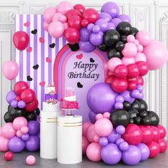 a birthday cake surrounded by balloons and streamers in front of a party arch with a sign that says happy birthday