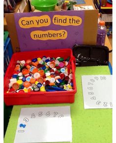 a red container filled with lots of colorful buttons next to a sign that says can you find the numbers?