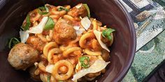 a brown bowl filled with pasta and meatballs on top of a table next to a rug