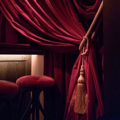 a red curtain with tassels hanging from it's side and two stools in front