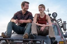 a man and woman sitting on the back of a pick - up truck smiling at each other