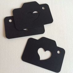 three black tags with hearts cut out of them on a white surface, one has a hole in the middle