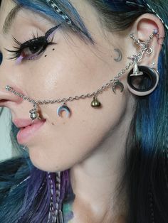 a woman with blue hair has piercings on her nose and ear chains attached to her ears