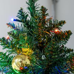 a close up of a christmas tree with lights on it's branches and a bauble ornament hanging from the top