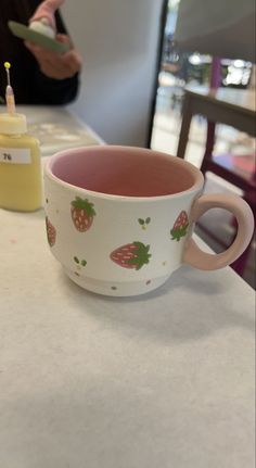 a coffee cup with strawberries on it sitting on a table next to a candle