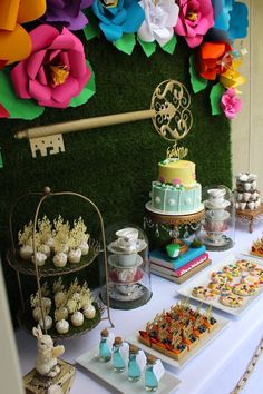 a table topped with lots of cakes and cupcakes next to a green wall