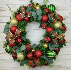 a christmas wreath with ornaments and greenery on a white wooden background, hanging from the wall