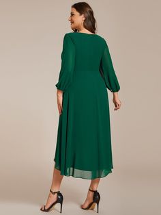 a woman wearing a green dress with long sleeves and pleaed heming on the waist