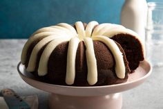 a chocolate bundt cake with white icing on a plate next to a bottle of milk