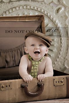 a baby in a suit case with a tie and hat on it's head