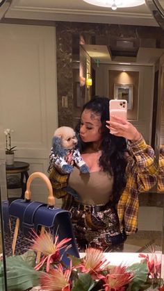 a woman taking a selfie in front of a mirror holding a small dog and wearing a plaid shirt