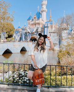 a woman is posing in front of a castle with her hat on and holding a suitcase