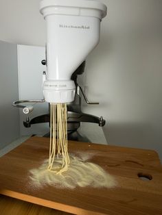 a white mixer is being used to make pasta on a cutting board with flour coming out of it