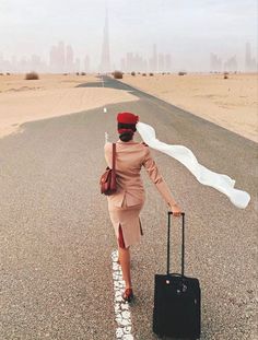 a woman walking down the road with her suitcase and scarf around her neck, in front of a cityscape