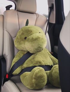 a green stuffed animal sitting in the back seat of a car with its head down