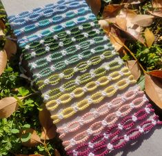 a crocheted scarf is laying on the ground next to some leaves and grass