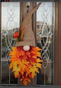 a scarecrow door hanger with fall leaves and an egg in it's mouth