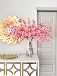 a vase filled with pink flowers sitting on top of a white table next to a mirror