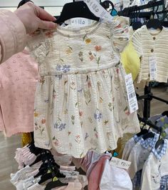 a person holding up a baby's dress in front of clothes on display at a store