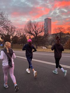 three people running down the street in front of a pink and blue sky at sunset