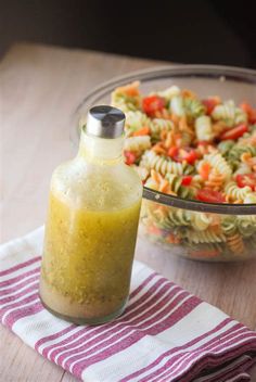 a bowl of pasta salad next to a bottle of dressing on a table with a towel